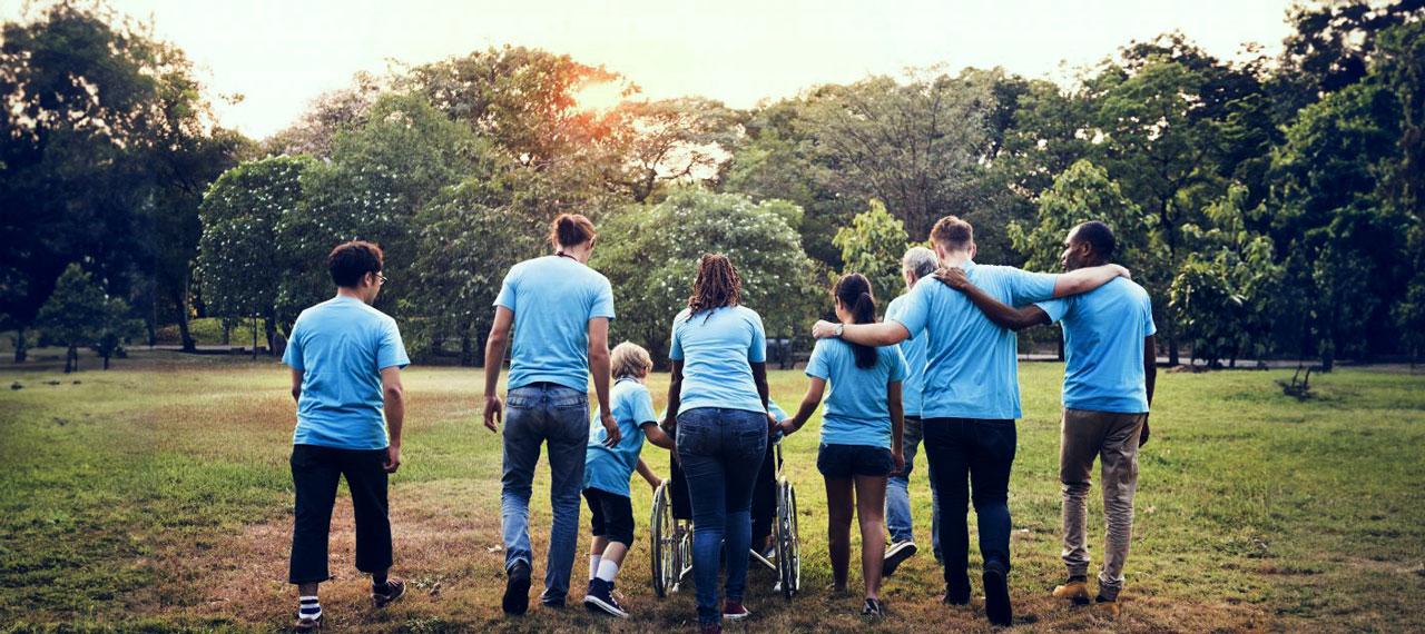 Groupe d’adultes et d’enfants vus de dos dans un parc, ils s’éloignent en marchant, ils portent tous un t-shirt bleu clair, une des personnes est en fauteuil roulant