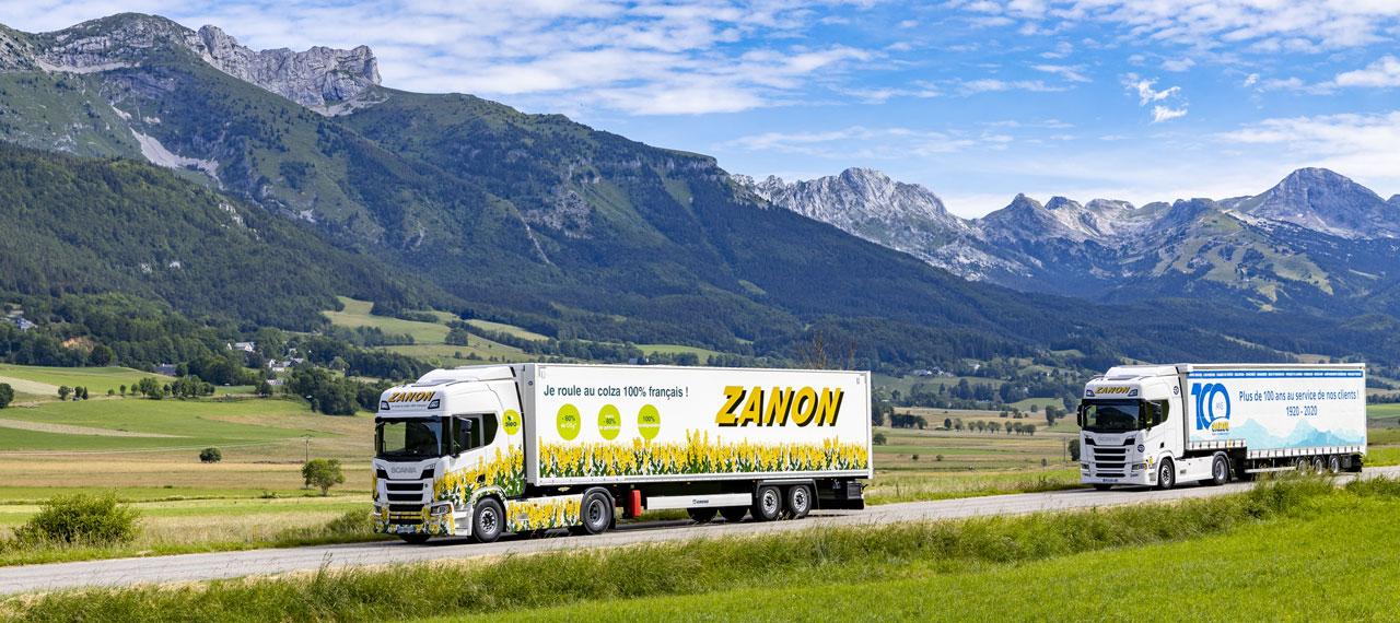 Camions de l’entreprise Zanon sur une petite route avec une chaine de montagne au loin 