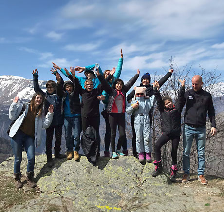 Association locomotive : un groupe d’enfants accompagné d’un adulte, ils ont tous les bas en l’air. On aperçoit la montagne enneigée au fond.