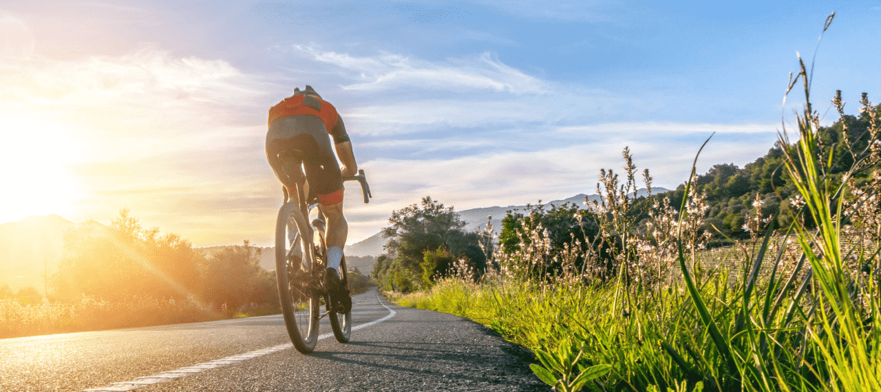 cycliste roulant sur une route avec en fond un paysage de montagne et un coucher de soleil