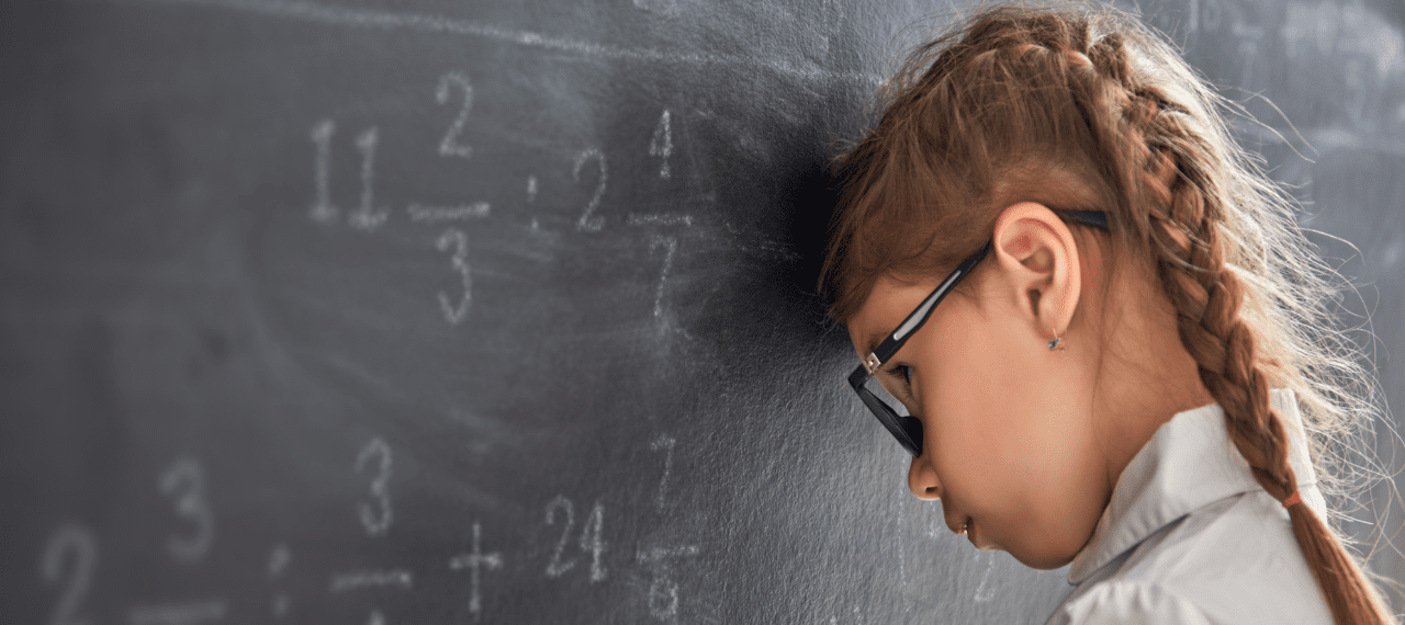 petite fille de dos la tête posée contre le tableau noir de la classe