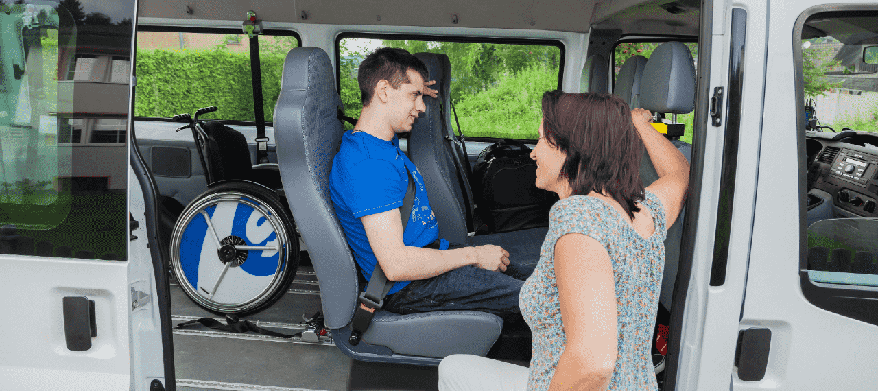 Jeune homme dans un minibus adapté avec une accompagnatrice à l'extérieur