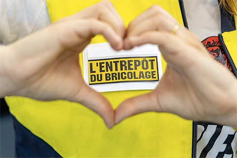 Mains faisant le signe du cœur ; le logo de L'Entrepôt du Bricolage est visible au centre du cœur