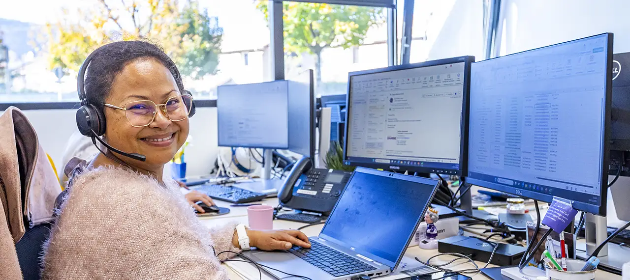 Femme travaillant devant plusieurs écrans, elle est souriante et regarde le spectateur