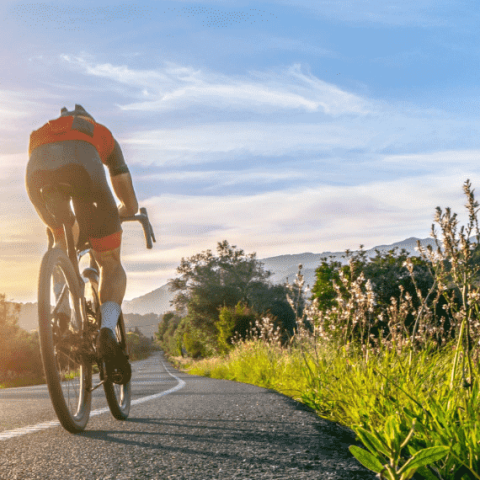 cycliste roulant sur une route avec en fond un paysage de montagne et un coucher de soleil