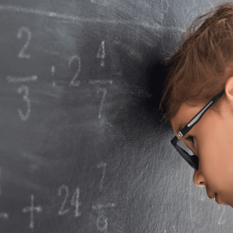 petite fille de dos la tête posée contre le tableau noir de la classe