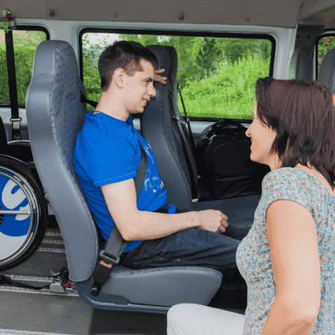 Jeune homme dans un minibus adapté avec une accompagnatrice à l'extérieur