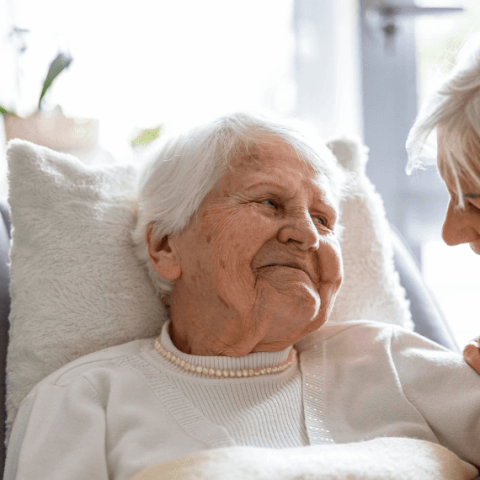 femme âgée sur un lit avec son aidante qui l'écoute